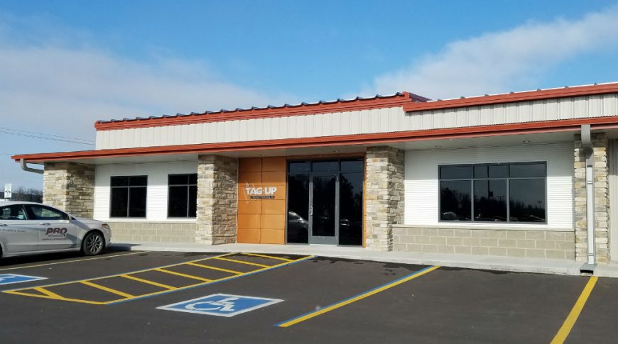 Entrance of beige and white metal building with brickwork columns and red gutters with brown panel accents.