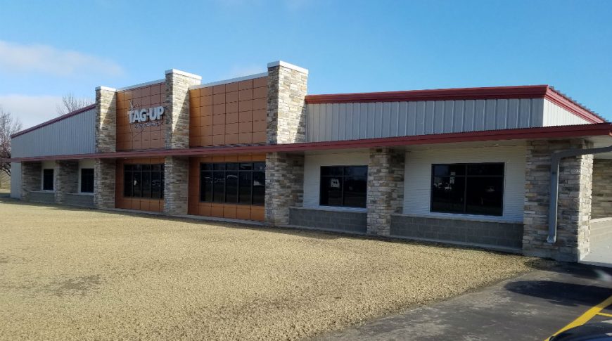 Side of Tag-Up building with light tan metal siding, brickwork column accents, and brown panels.