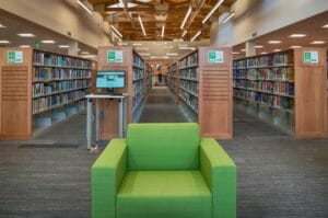 Bright green chair followed by rows of bookshelves behind and a beautiful wood trussed ceiling above.