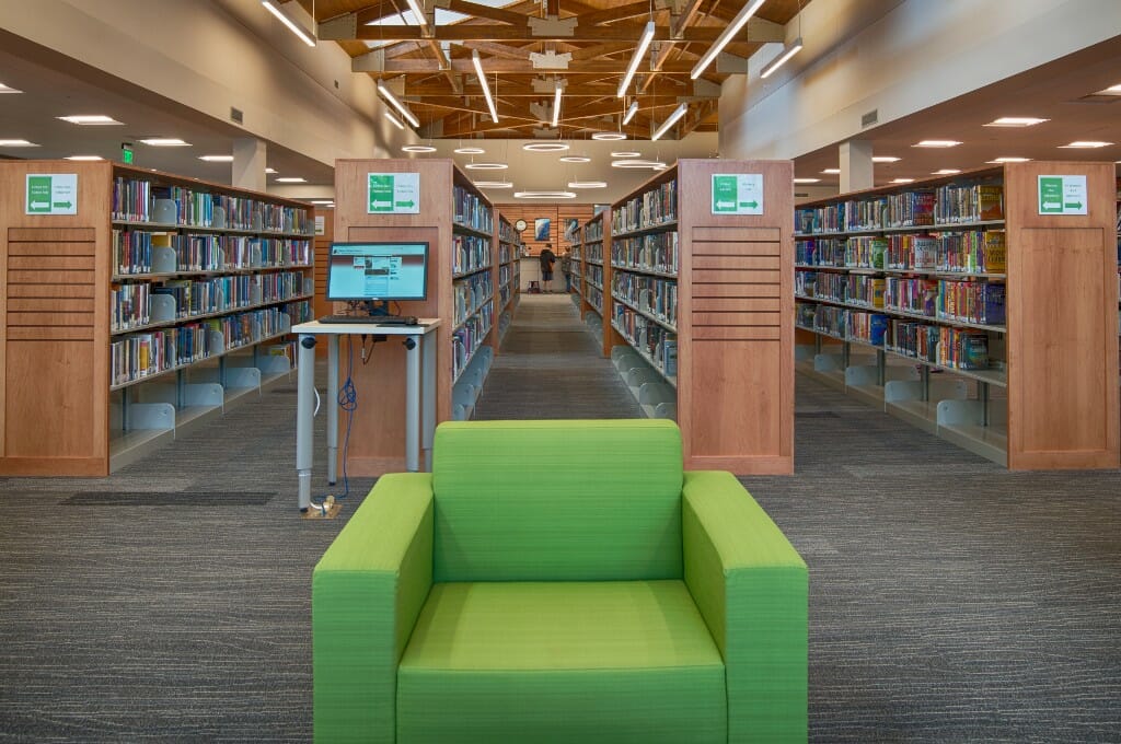 Bright green chair followed by rows of bookshelves behind and a beautiful wood trussed ceiling above.