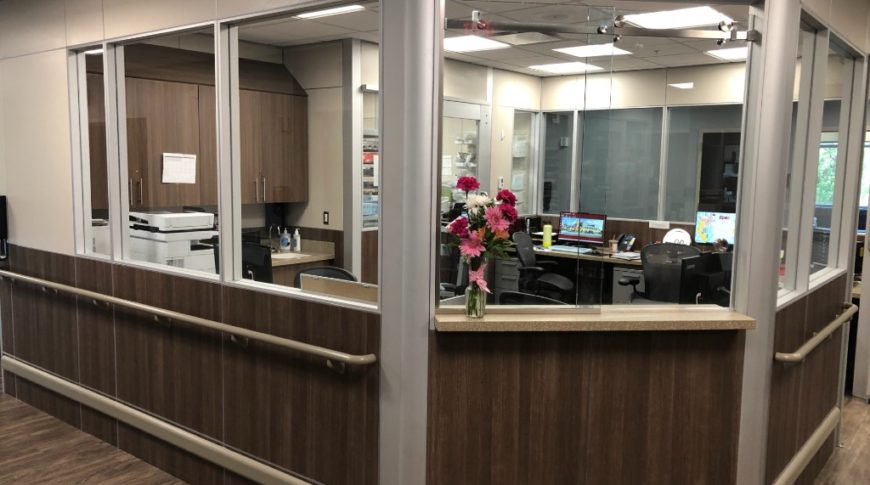 Corner view of a new reception station with dark wood paneling on the bottom half of the wall mirrored by light beige walls above and windows looking in to the registration station.