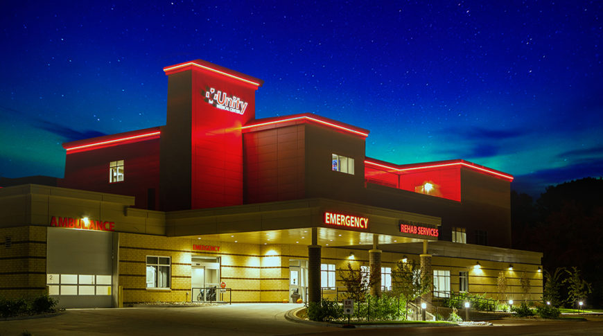 Night snapshot of the outside of the Unity Medical Center building showcasing neon lit signs for the Emergency, Ambulance, and Rehab Services entrances.