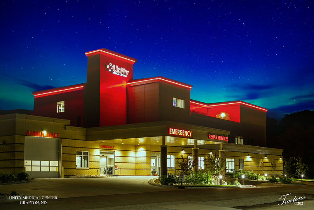 Night snapshot of the outside of the Unity Medical Center building showcasing neon lit signs for the Emergency, Ambulance, and Rehab Services entrances.