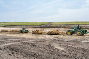Two green tractors pulling earthwork machines in dirt field