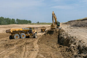 Excavator digging up dirt in bare field to load on to dump trucks
