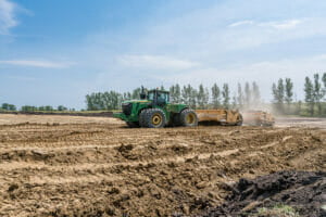 Green tractor pulling dirtwork implement in bare dirt field