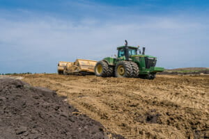 Green tractor pulling dirt work implement in dirt field