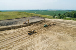 Aerial view of dirt field with excavator, dump truck, and tractor implements