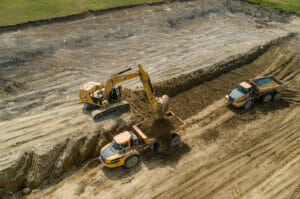 Aerial view of an excavator dumping dirt in a dump truck in a dirt field