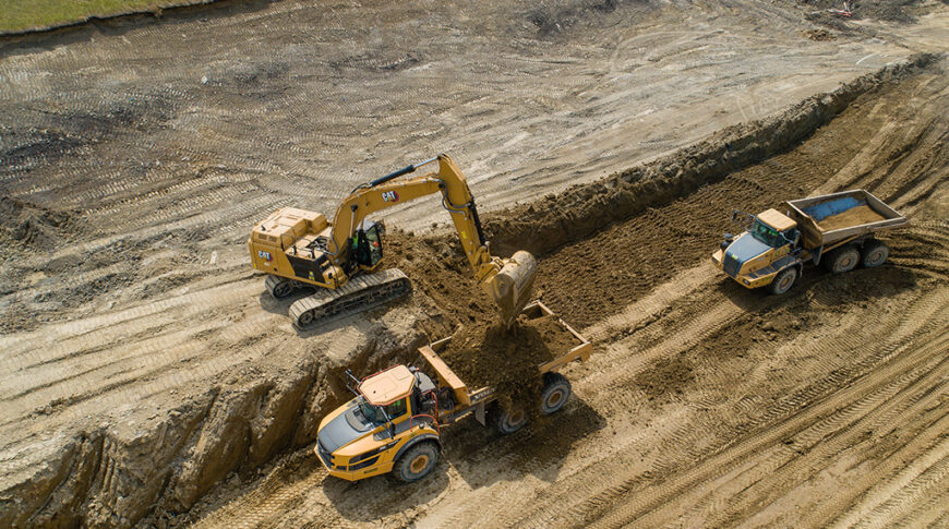 Aerial view of an excavator dumping dirt in a dump truck in a dirt field