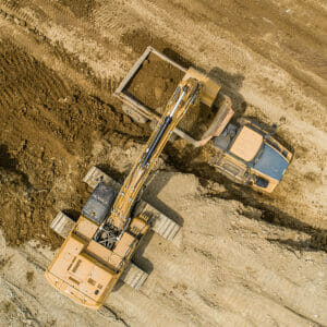 Aerial view straight overhead of excavator loading dirt into dump truck in dirt field