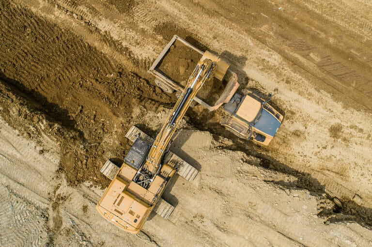 GwinnerLandfill-0059- Civil Construction Aerial view straight overhead of excavator loading dirt into dump truck in dirt field