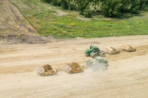 Aerial view of two green tractors with dirt work implements in dirt field