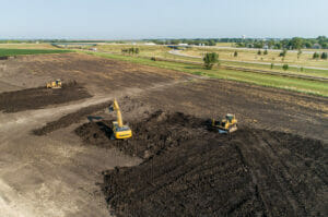 Aerial view of an excavator and two bulldozers clearing a dirt field