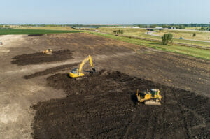 Aerial view of an excavator and two bulldozers clearing a dirt field