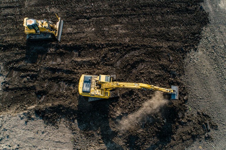 Bird's eye view of an excavator and bulldozer digging in a dirt field