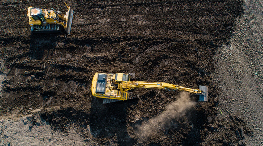 Bird's eye view of an excavator and bulldozer digging in a dirt field