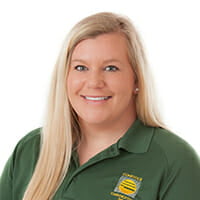 Woman with light skin and long blonde hair and green Comstock Construction polo sitting for portrait