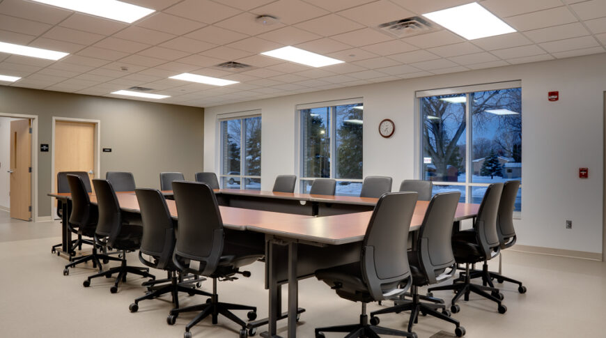 Conference room with rectangular table and office chairs surrounding it.