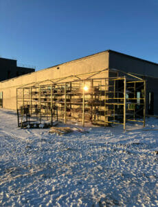 Scaffolding wrapping around the corner of a brick building on a snowy, sunny morning.