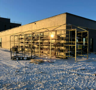 Scaffolding wrapping around the corner of a brick building on a snowy, sunny morning.