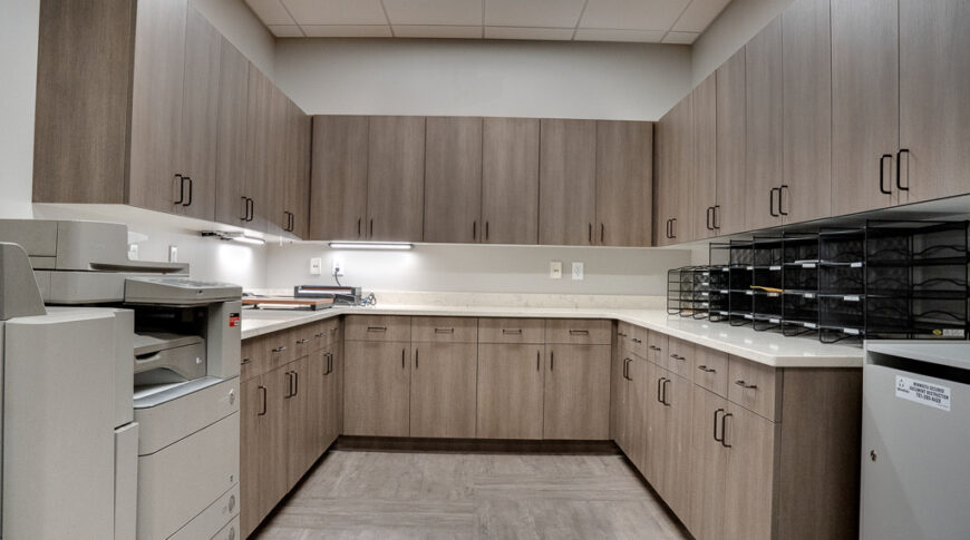 U-shaped copy room with upper and lower cabinetry on three walls and printer machine on upper left side.