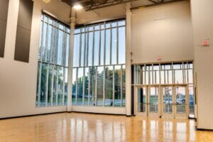 Corner of gymnasium with floor to ceiling two-story windows wrapping around the corner with glass exit doors to the right.