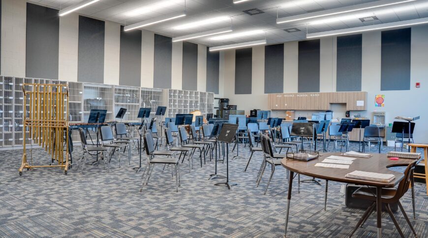 Two-story tall band room with chairs and music pedestals throughout with percussion instruments in the back row.