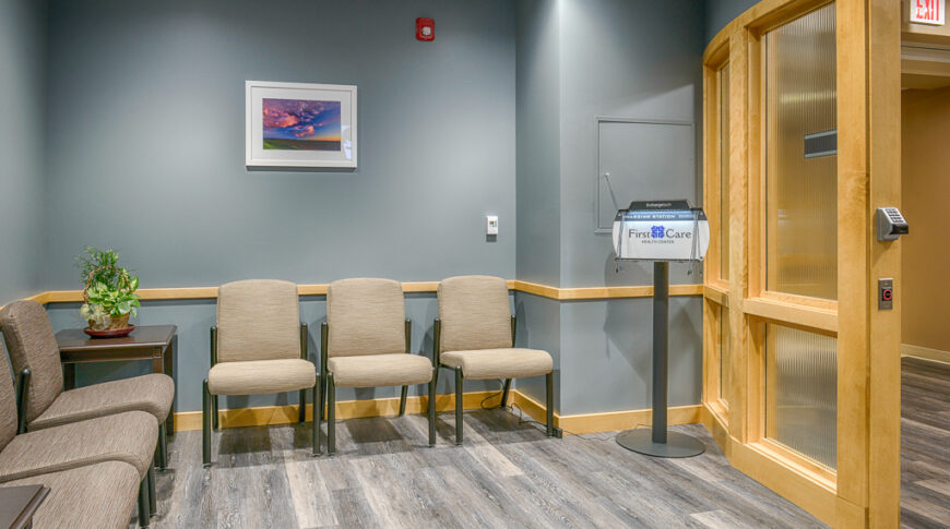 Hospital waiting room with steel blue/gray walls, maple wood finishes and chairs on back walls.