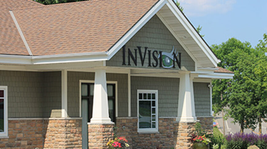 Exterior view of InVision eye clinic with green shaker siding, white and stone columns and brown shingled roof.