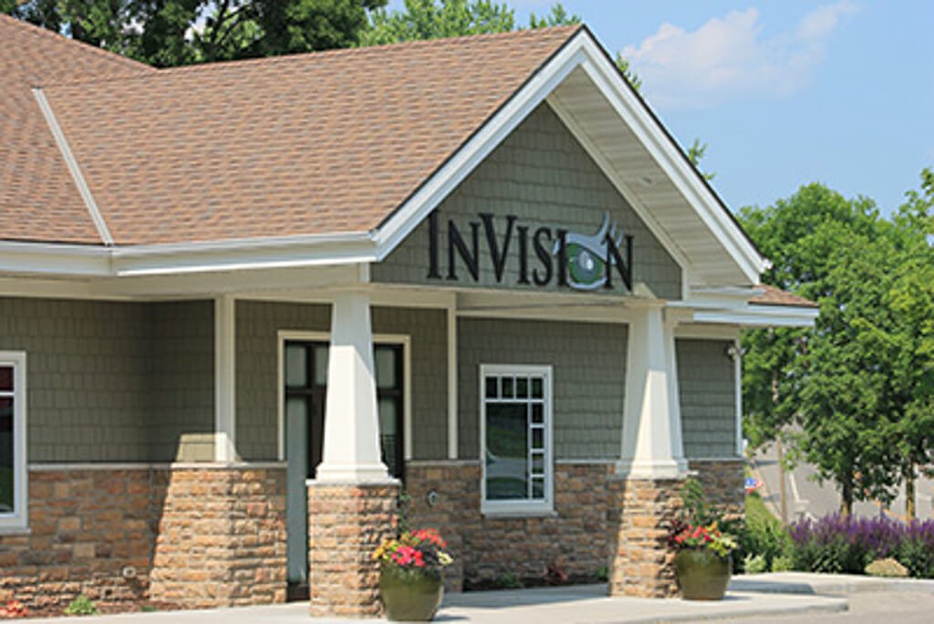 Exterior view of InVision eye clinic with green shaker siding, white and stone columns and brown shingled roof.
