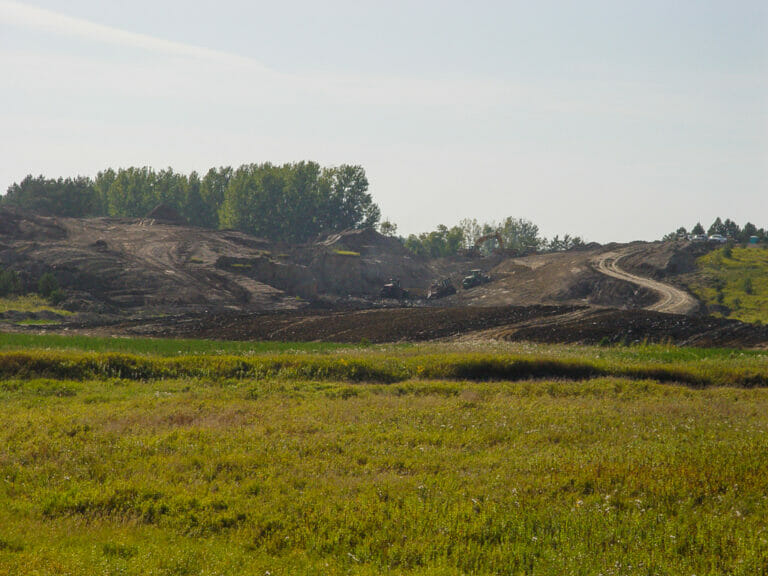 Lake LaMoure Spillway-Civil Construction-Low Res-1 Scenic landscape of lush green wild-grown field in foreground followed by dirt field with machinery moving dirt up small hill in background.
