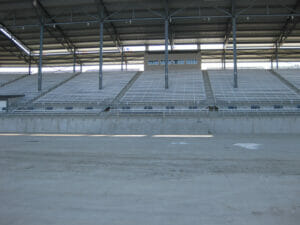 Track view of concrete ND State Fair Grandstands base with metal bleachers and steel beams upholding metal roof above.