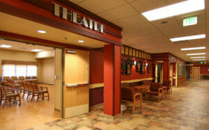 Hallway with double doors leading to room with wooden flooring and chairs throughout with an archway above and a sign that says 'Theatre."
