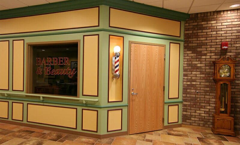 Interior of senior care building that has faux barbershop façade with barbershop sinning light and window that says "Barber & Beauty."