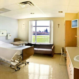 Hospital room with bright sunny window on back wall, bed and couch in foreground.
