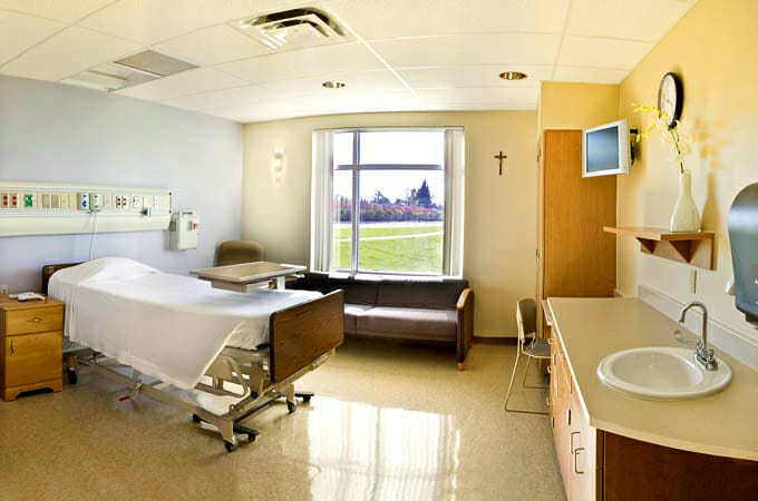 Hospital room with bright sunny window on back wall, bed and couch in foreground.