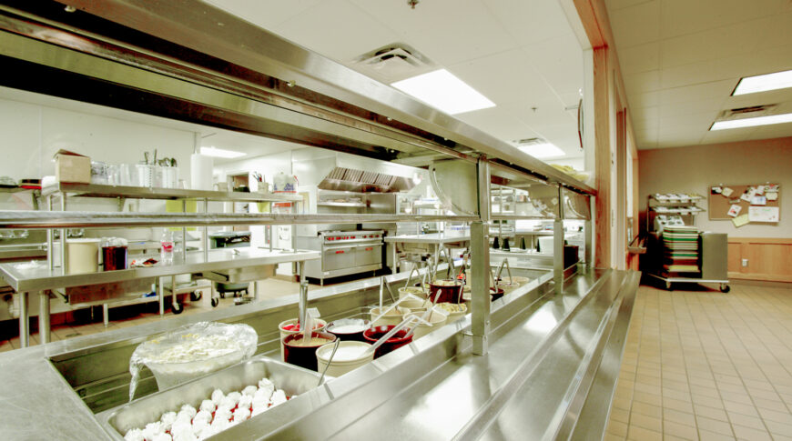 Commercial kitchen with pass-through window to tiled dining hall.