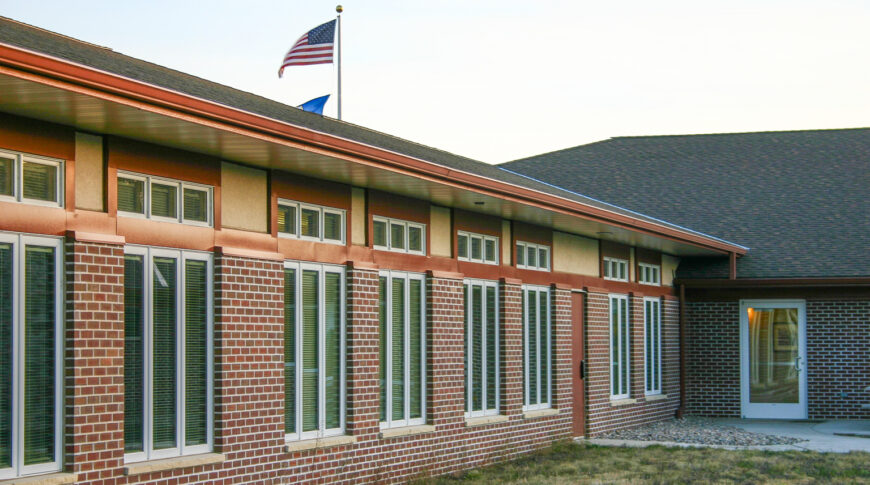 Exterior view of red-bricked building with long tall windows spaced every few feet.