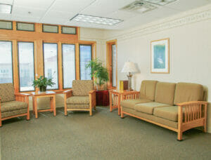 Living room area with tall windows on back wall and seating couch and chairs throughout.