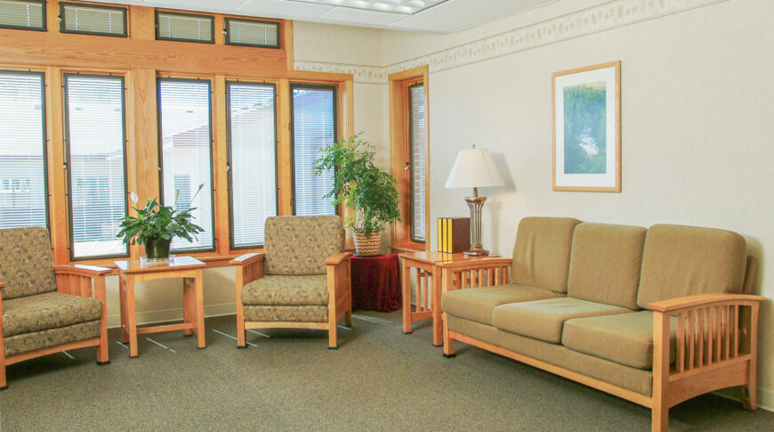 Living room area with tall windows on back wall and seating couch and chairs throughout.