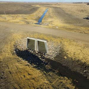 Large storm drain underneath gravel road. Rock checks on either side and beneath to reduce erosion.