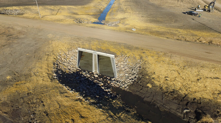 Large storm drain underneath gravel road. Rock checks on either side and beneath to reduce erosion.