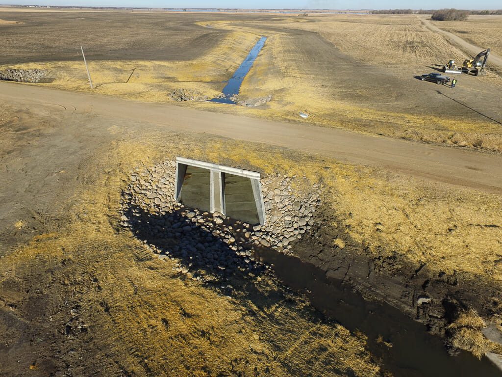 Large storm drain underneath gravel road. Rock checks on either side and beneath to reduce erosion.