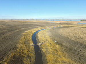 Aerial view of drainage channel snaking through brown dirt fields with rock check leading out of new concrete reinforced box culverts
