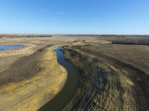 Aerial view of drainage channel snaking through brown dirt fields.