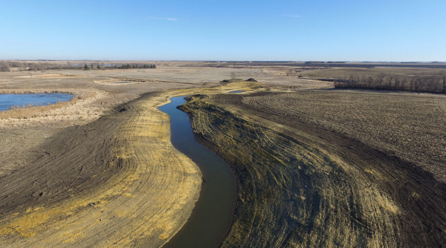 Aerial view of drainage channel snaking through brown dirt fields.