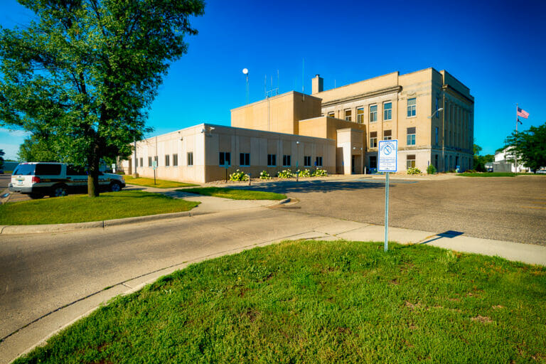 Precast concrete exterior entrance view of Wilkin County Jail building connected to the original government brick building to the right.