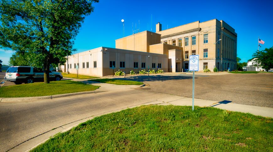 Precast concrete exterior entrance view of Wilkin County Jail building connected to the original government brick building to the right.