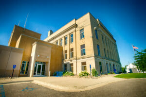 Precast concrete exterior entrance view of Wilkin County Jail building connected to the original government brick building to the right.